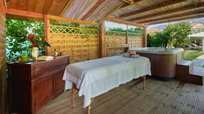 A wooden room with a bed, a wooden bench, a hot tub, and a wooden table with a vase of flowers.