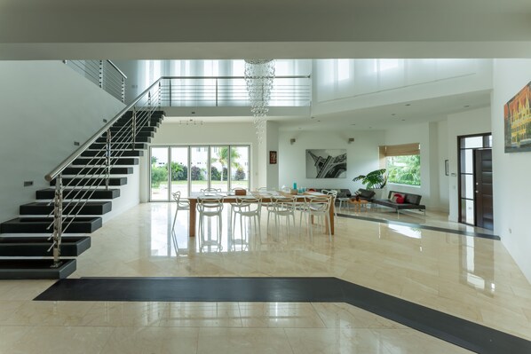Un intérieur spacieux et moderne, doté d’un escalier, d’un coin repas et d’une grande fenêtre offrant une vue sur la verdure.