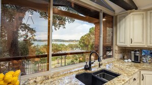 A kitchen with a granite countertop, a sink, and a view of a lake through large windows. - Hummingbird Hideaway - Canyon Lake Waterfront + Pool & Hot Tub + Game Room + Covered Patios (Canyon Lake)