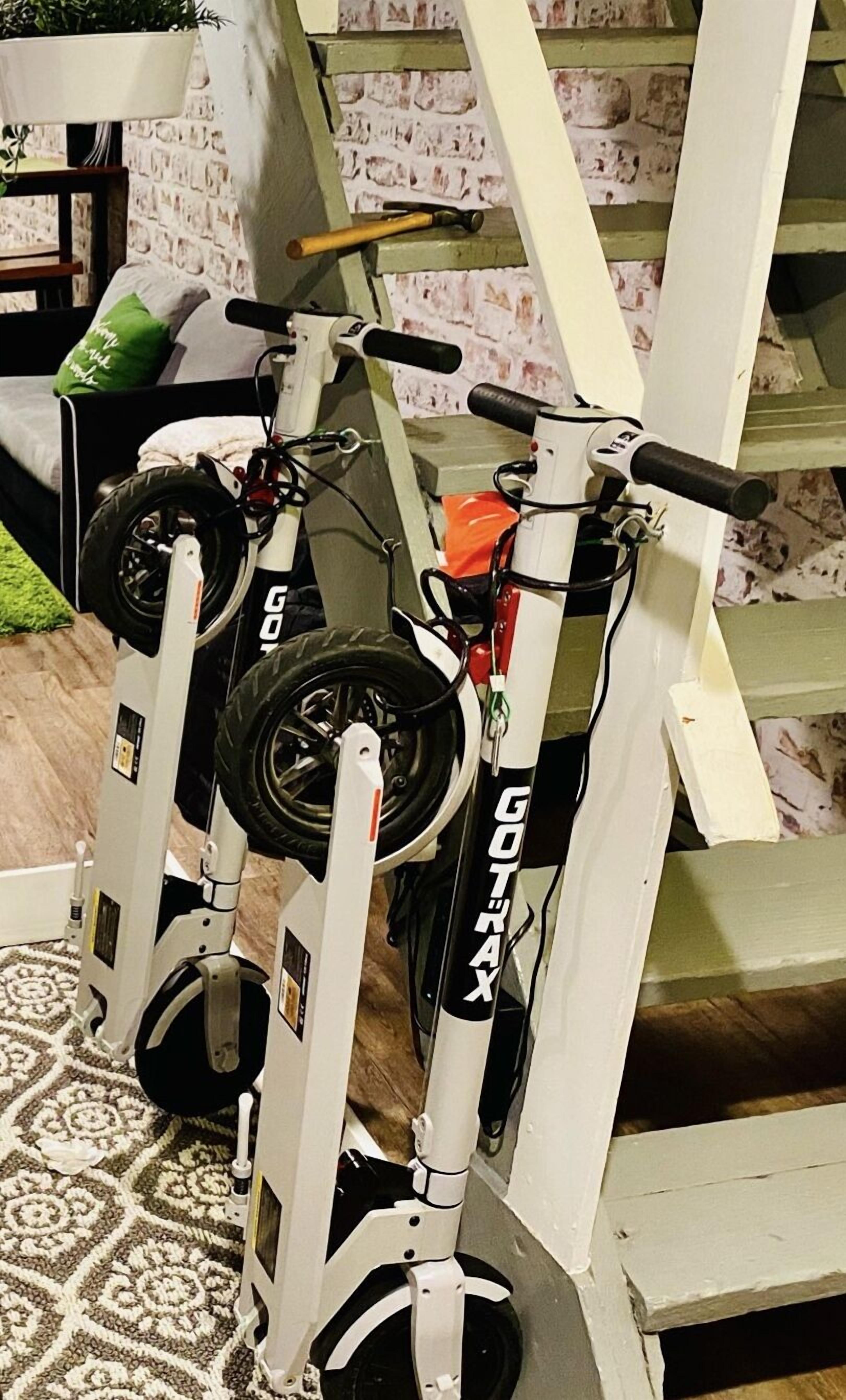 A stationary bike with a handlebar and two wheels, placed in a room with a patterned carpet and a brick wall.