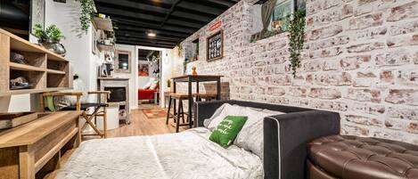A room with a bed, a wooden desk, a brick wall, and a window.