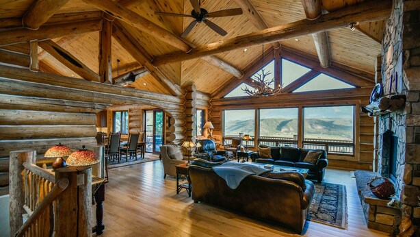 Un intérieur spacieux de chalet en bois, avec un plafond haut, de grandes fenêtres, une cheminée et un coin salon confortable.