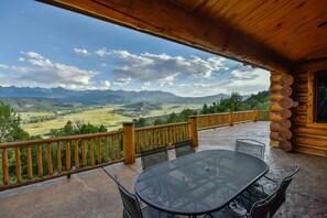 Une terrasse en bois avec une table et des chaises, offrant une vue sur un paysage montagneux.