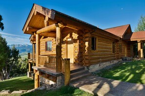 Une cabane en rondins avec un porche, des marches en pierre et une vue sur les montagnes.