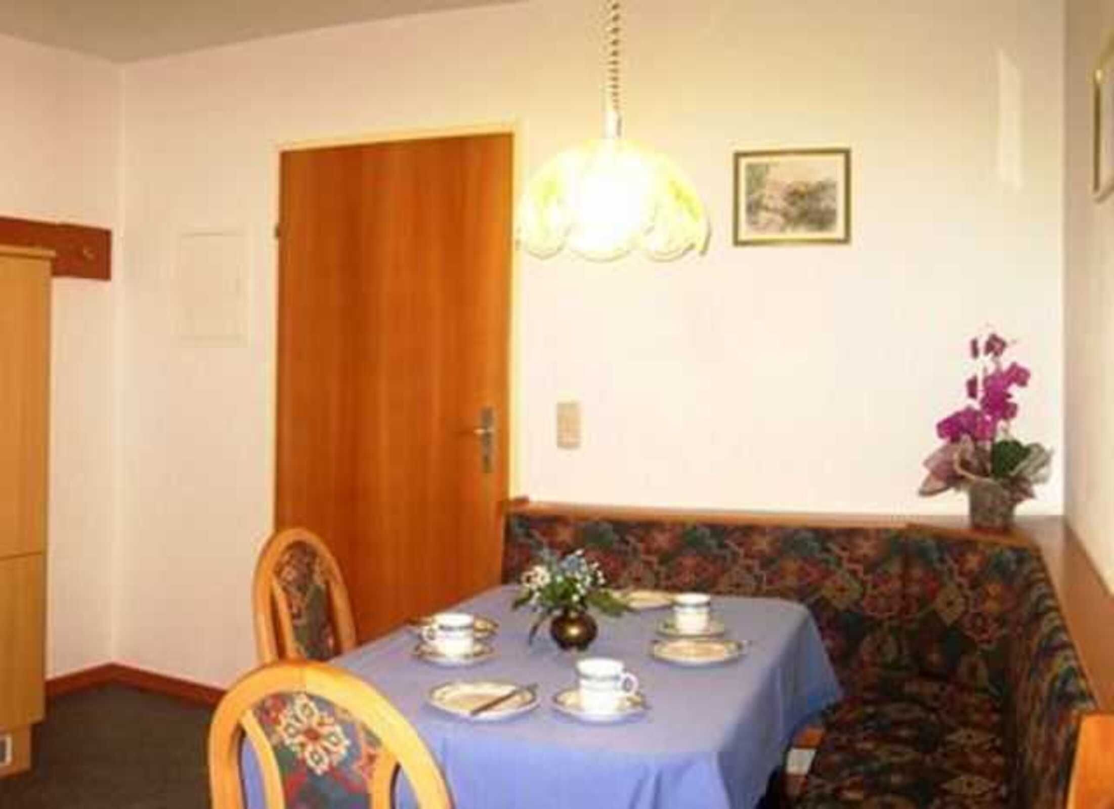 Un comedor con una mesa dispuesta para cuatro personas, un sofá floral, una puerta de madera y una lámpara colgante.