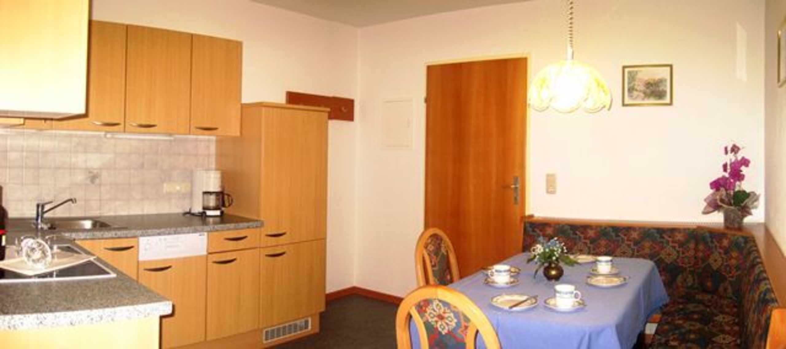 A compact kitchen with wooden cabinets, a dining table set with plates, and a patterned sofa.