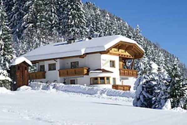 Una cabaña cubierta de nieve con fachada de madera y un balcón grande.