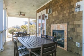 Une terrasse couverte avec une table et des chaises en bois, une cheminée et une vue sur les maisons voisines.