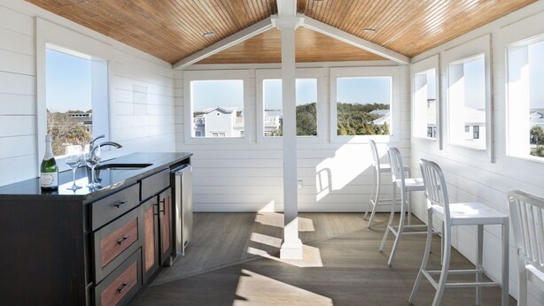 Une cuisine moderne avec un plafond en bois, de grandes fenêtres et un coin bar avec des chaises blanches.