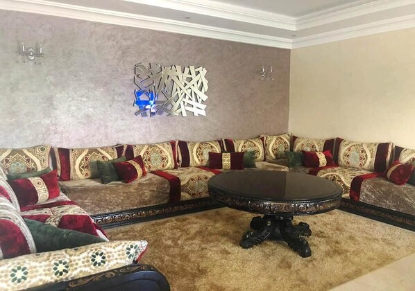 A living room with a patterned sofa set, a round coffee table, and a decorative wall piece. - Sublime Beachfront Villa in Savannah Beach 4522 (Sidi Rahal)