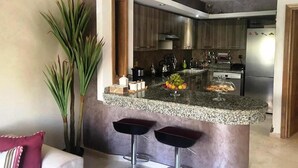 Une cuisine moderne dotée de plans de travail en granit, d’appareils électroménagers en acier inoxydable et d’un îlot central avec des tabourets de bar.