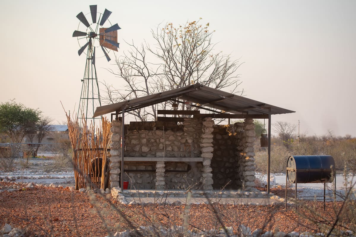 A rustic stone building with a metal roof and a windmill nearby.