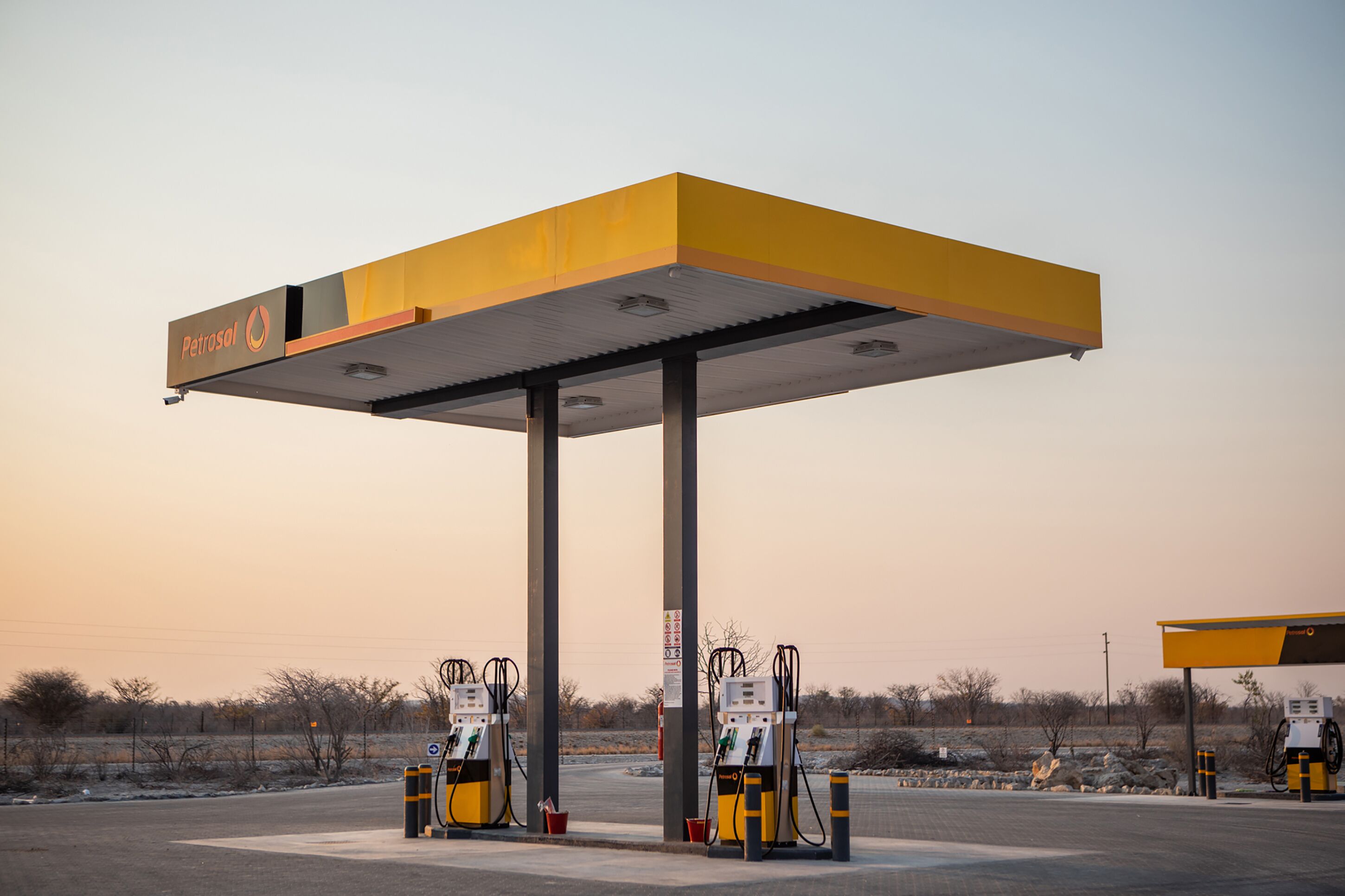 Una estación de servicio con toldo amarillo, varias bombas de combustible y cielo despejado.