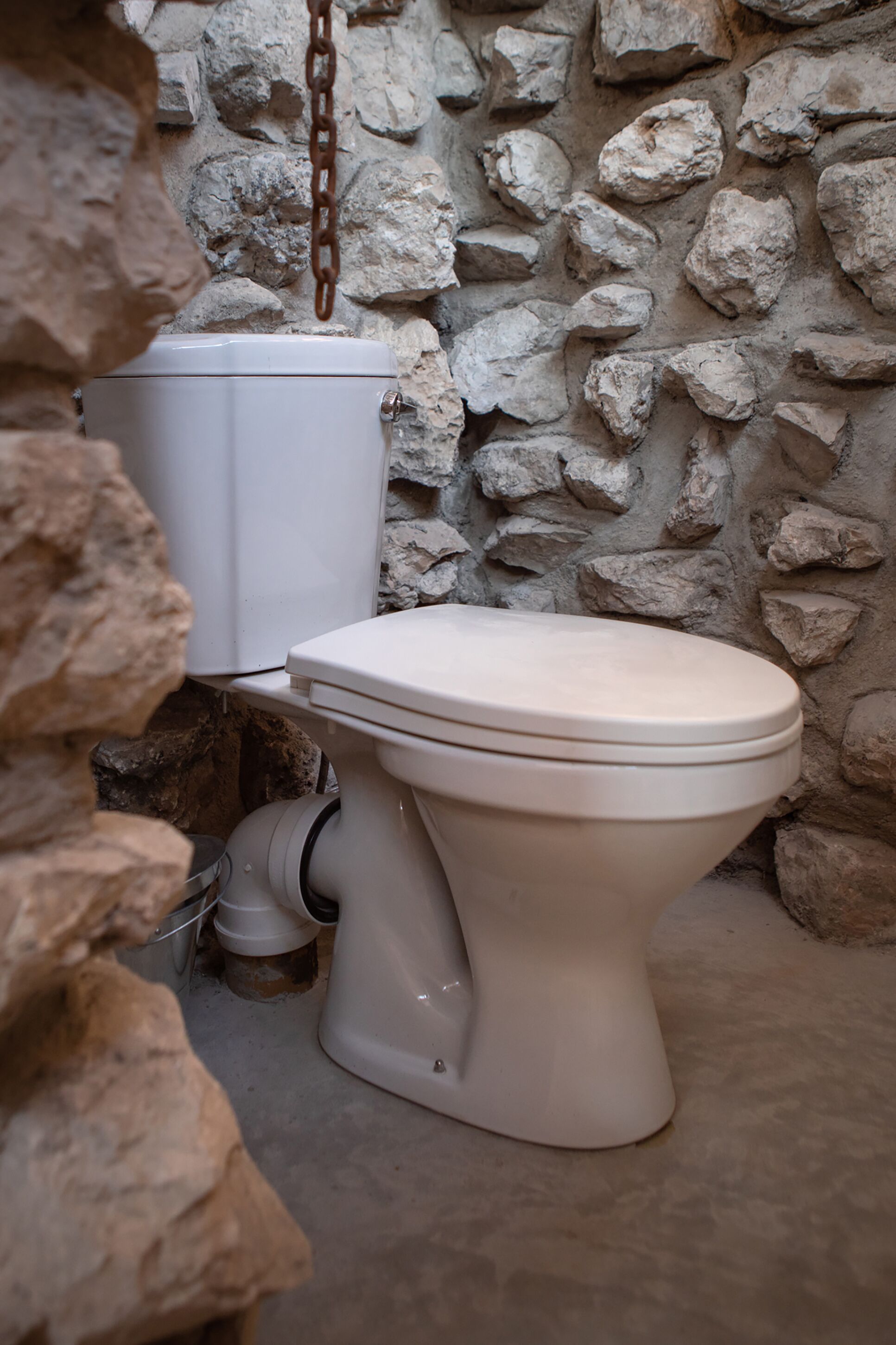 A toilet in a stone-walled bathroom.