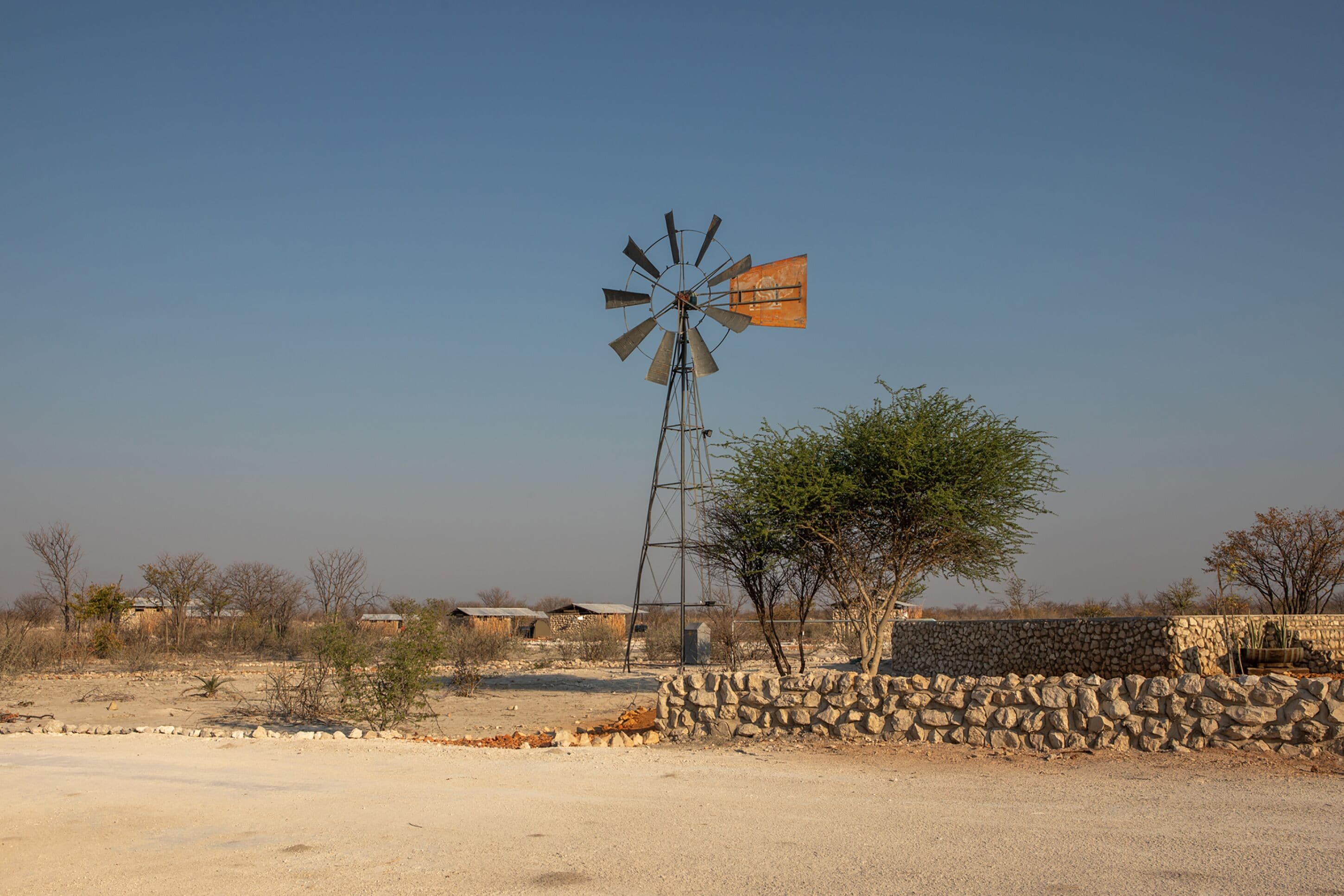 Un molino de viento en un entorno rural, con un muro de piedra y vegetación escasa.