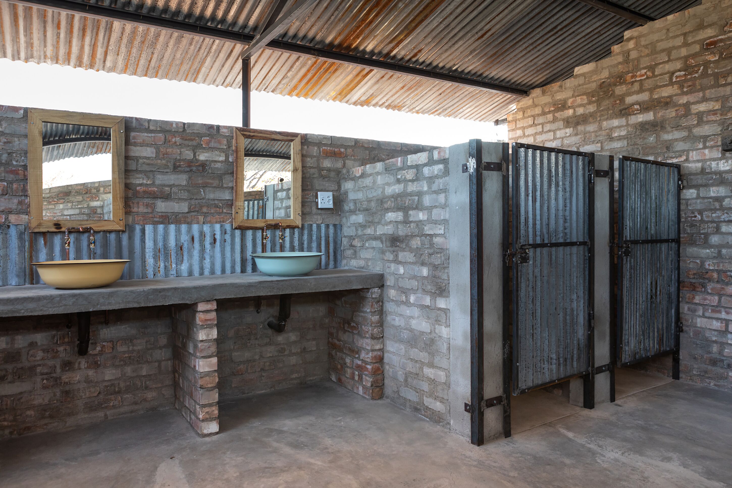 A rustic bathroom with a concrete sink, a wooden-framed mirror, and metal doors.