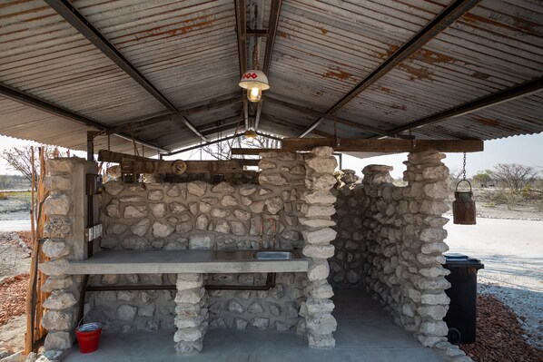 A stone-built outdoor kitchen with a metal roof, a sink, and a hanging lantern. - Etosha Trading Post (Okaukuejo)