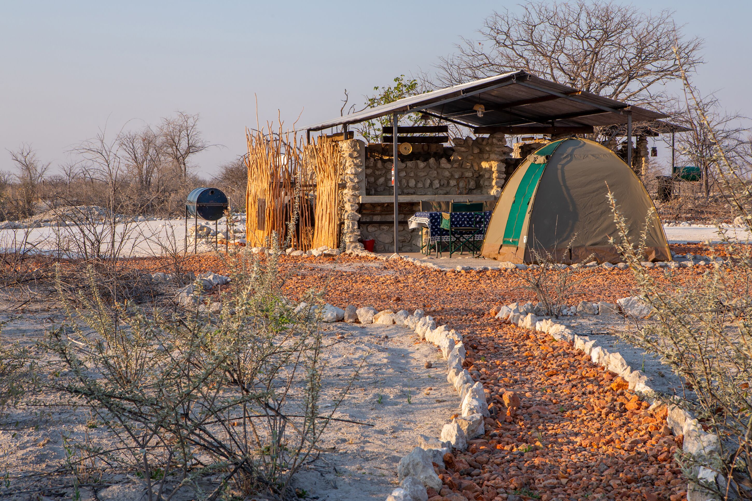 Une cabane rustique aux murs en pierre, avec un toit en métal, et une tente installée à proximité.