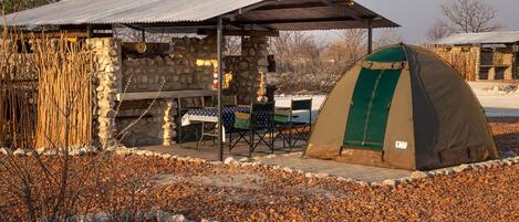 A rustic campsite with a stone building, a covered picnic table, and a tent.