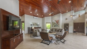A spacious living room with a large flat-screen TV, a wooden ceiling, and a fireplace. - New Luxury Home, private pool! 300 steps to beach, 8 min. walk to bars & dining (Dominical de OSA)