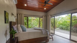 A bedroom with a wooden ceiling, large windows, a bed with pillows, and a plant on a nightstand. - New Luxury Home, private pool! 300 steps to beach, 8 min. walk to bars & dining (Dominical de OSA)