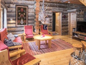 Interior de una cabaña de troncos con una zona de estar acogedora, una mesa de madera y una chimenea.