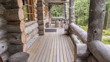 A log cabin with a wooden deck, large windows, and a view of the forest.