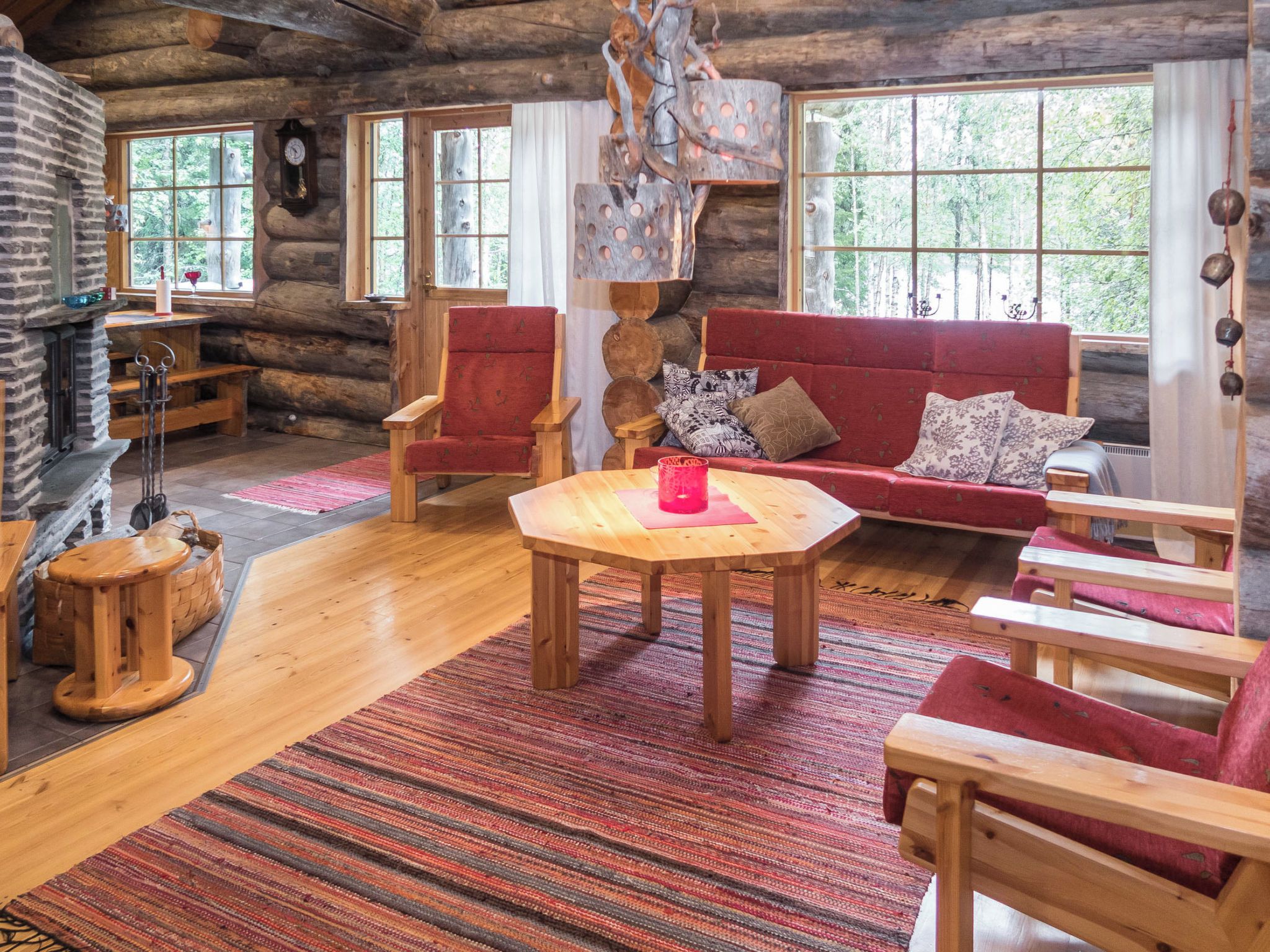 A log cabin interior with a wooden dining table, red upholstered chairs, a red sofa, and a fireplace.