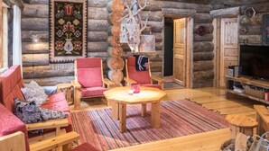 Ein gemütliches Blockhaus-Interieur mit einem Holzespeise-Tisch, roten Polsterstühlen, einer Couch und einem Fernseher.