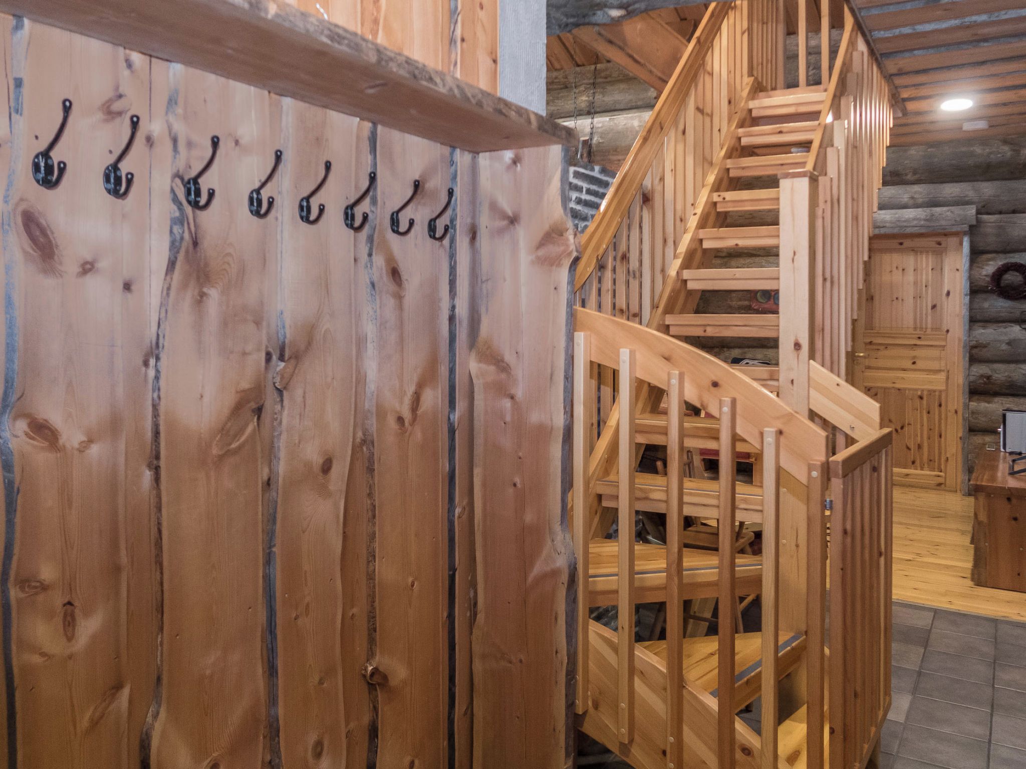 Una escalera de madera con barandilla que conduce a un nivel superior, una pared de madera con varios ganchos y un suelo de madera.