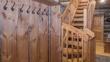 Una escalera de madera con barandilla que conduce a un nivel superior, una pared de madera con varios ganchos y un suelo de madera.