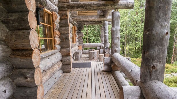 Eine Blockhütte mit einer Holzdielen-Terrasse und großen Fenstern.