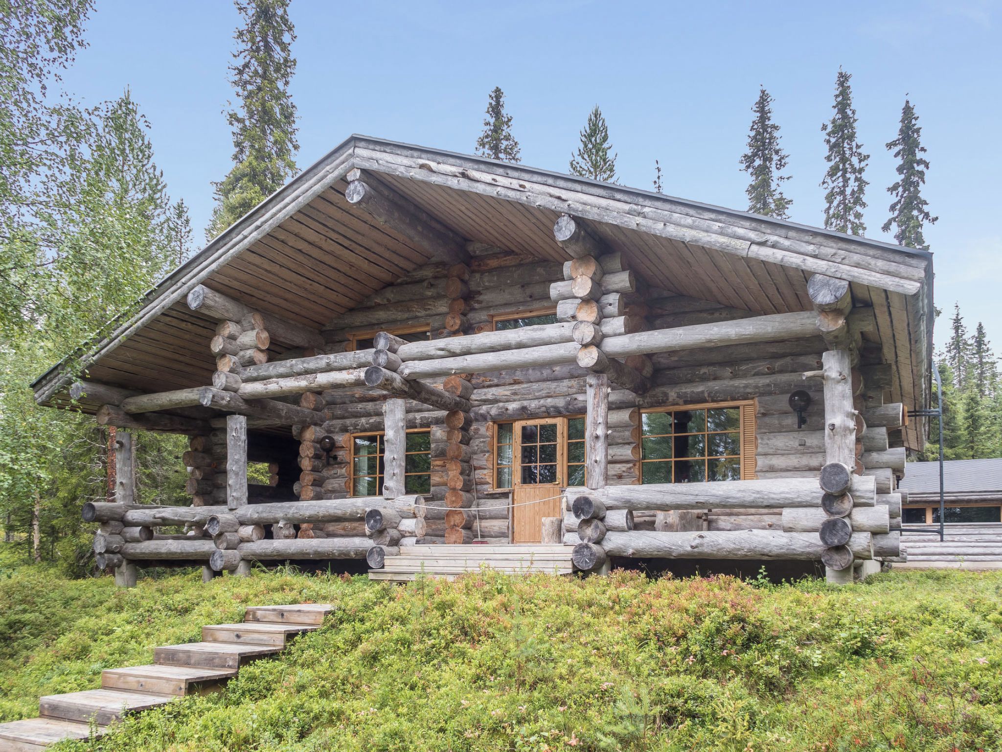 A log cabin with a porch, wooden steps, and a clear view of the surrounding forest.
