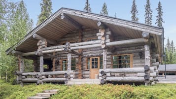 A log cabin with a porch, wooden steps, and a clear view of the surrounding forest.