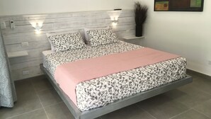 Ein modernes Schlafzimmer mit grauem Holz-Kopfteil, zwei Wandleuchten, einer gemusterten Tagesdecke und einer rosafarbenen Decke.