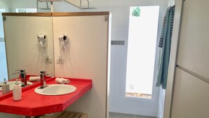 Ein Badezimmer mit roter Arbeitsplatte, zwei Waschbecken, einem Spiegel, einer Dusche und einer Tür, die nach draußen führt.