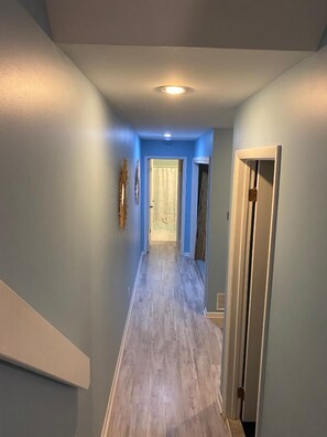 Un couloir aux murs bleu clair, avec un plancher en bois et une porte au fond.