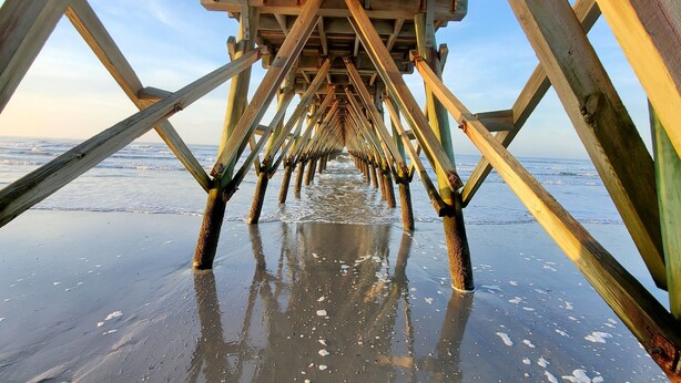 Una estructura de muelle de madera con una vista despejada de la playa y el océano al fondo.