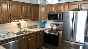 Una cocina con armarios de madera, electrodomésticos de acero inoxidable, lavavajillas y cafetera.