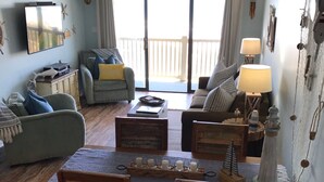 Una sala de estar acogedora con una mesa de comedor, sillas y un sofá. Hay un letrero que dice "BEACH HOUSE" sobre la puerta.