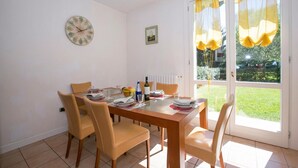A dining area with a wooden table, four chairs, a clock, and a window with curtains. - Porto Letizia Mimosa 2, Porlezza, Italy (Porlezza)