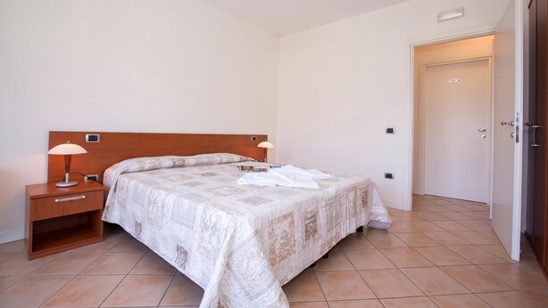 Une chambre à coucher avec un lit, des tables de chevet, une porte et un sol carrelé.