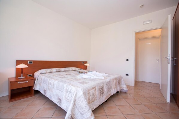 A bedroom with a bed, nightstands, a door, and a tiled floor. - Porto Letizia S4, Porlezza, Italy (Porlezza)