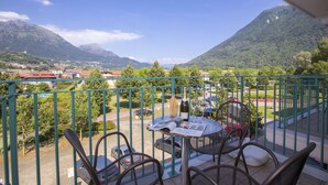 Un balcon avec une table et des chaises, donnant sur un paysage montagneux et offrant une vue sur une ville et la verdure environnante.