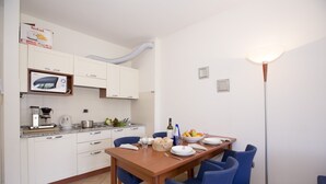 Une cuisine moderne avec des meubles blancs, un four à micro-ondes et une machine à café. On y trouve une table à manger avec des chaises et un lampadaire.