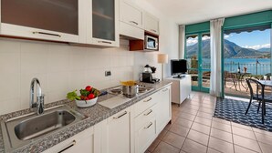 A modern kitchen with a sink, stove, and microwave, and a balcony with a view of the lake and mountains. - Porto Letizia P10, Porlezza, Italy (Porlezza)