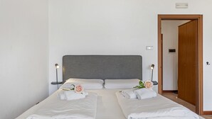 A neatly made double bed with white linens and two pink roses, bedside lamps, and a wooden door in the background. - Porto Letizia P10, Porlezza, Italy (Porlezza)