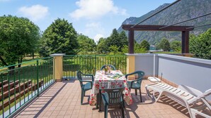 Une terrasse avec une table et des chaises, une pergola et une vue sur les montagnes et les arbres.