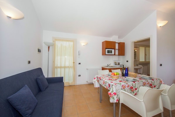 A compact living space with a sofa, dining table, chairs, a microwave, and a small kitchen area. - Porto Letizia Tulipano 7, Porlezza, Italy (Porlezza)