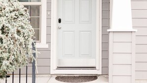A house with a white front door, a small porch, and a window with a white frame.